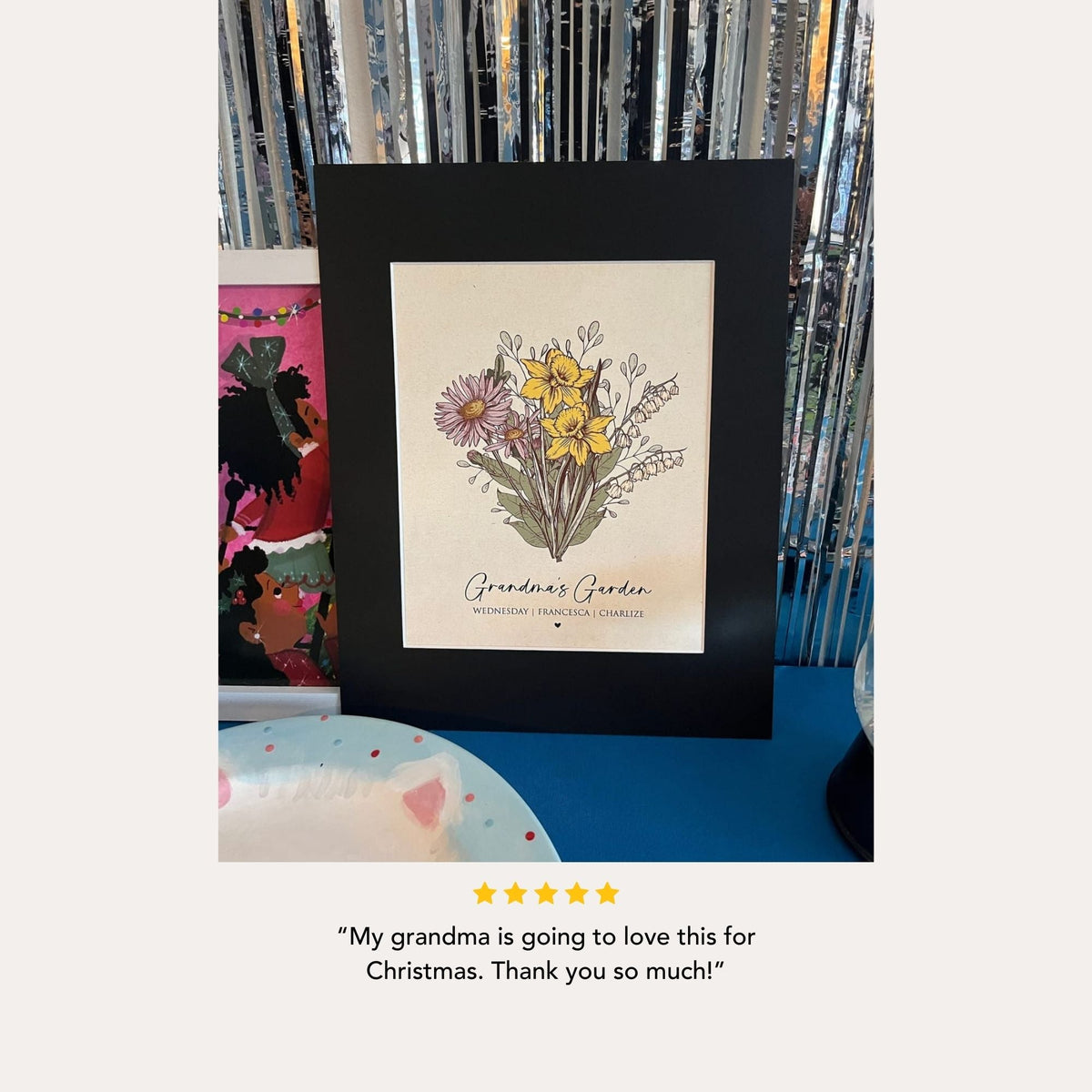 a framed print of a floral arrangement, placed on a table with a blue surface. The print is titled "Grandma's Garden" and has a rating of 5 stars. The text below the image reads, "My grandmother is going to love this for Christmas. Thank you so much!"